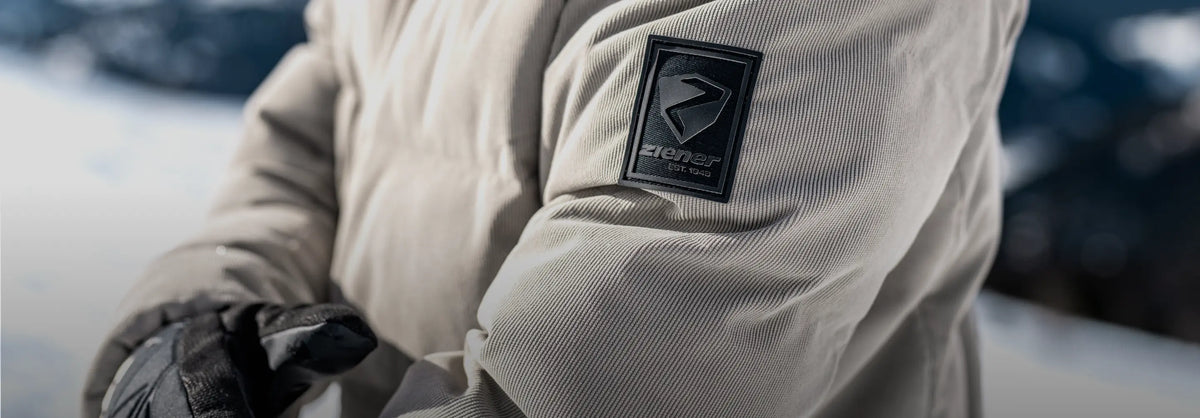 Nahaufnahme des ZIENER Logos am Ärmel einer beigen Skijacke