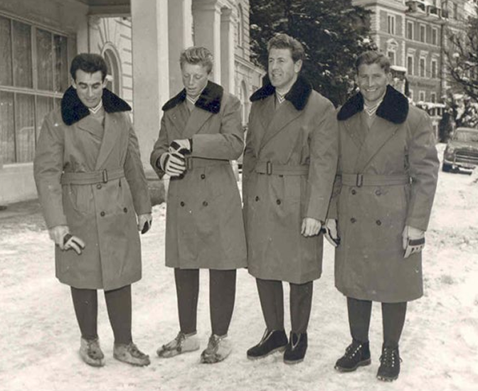 Historisches Schwarz-Weiß-Foto: vier Männer in Mänteln stehen im Schnee vor einem Gebäude