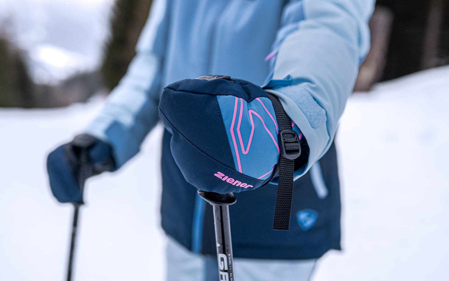 Kind in hellblauer Skijacke hält mit einem dunkelblauen ZIENER Fäustling einen Skistock