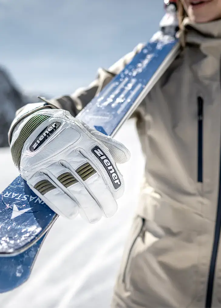 Hand in a white ZIENER ski racing glove holding a ski