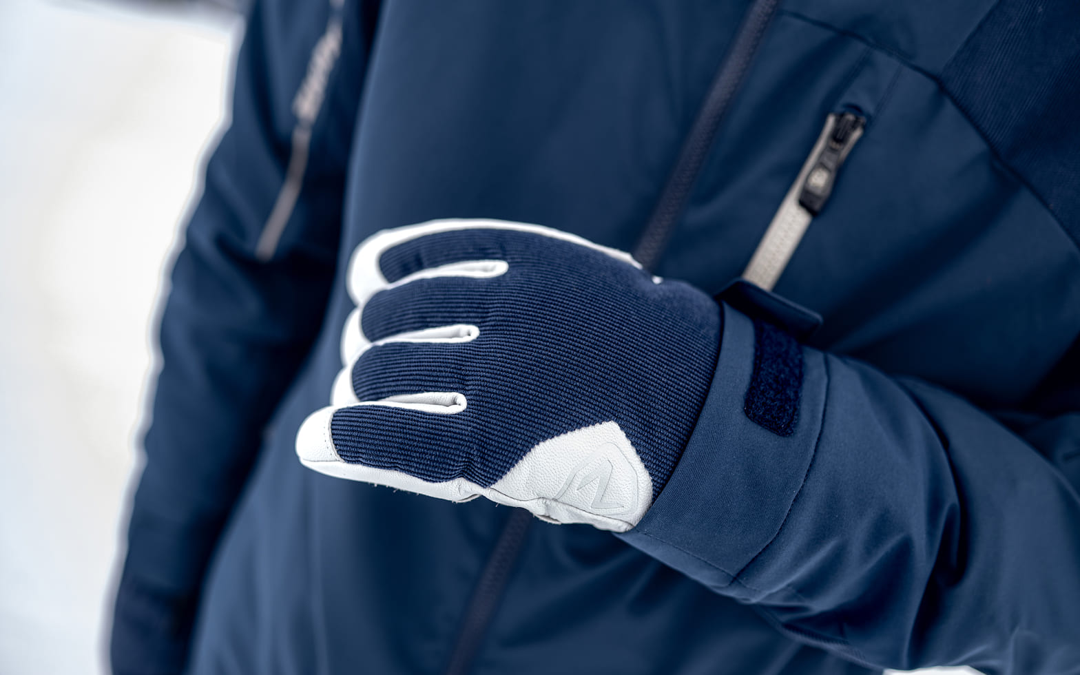 Nahaufnahme eines dunkelblau-weißen Skihandschuhs an einer dunkelblauen Skijacke