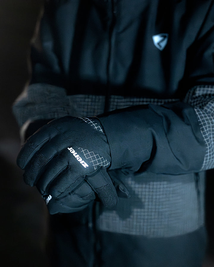 Close-up of black ZIENER gloves against a dark jacket with a reflective ripstop pattern